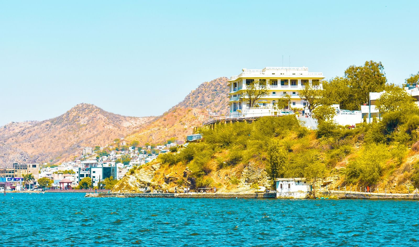 A scenic view of a bright blue lake with a building nestled on a hillside in the background.