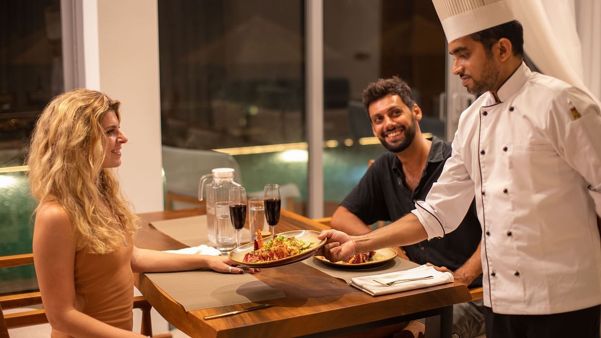 image of a chef serving well decorated plate of a sea food cuinsine to the couple at the the beacon by the bay villas and suites in dondra, sri lanka