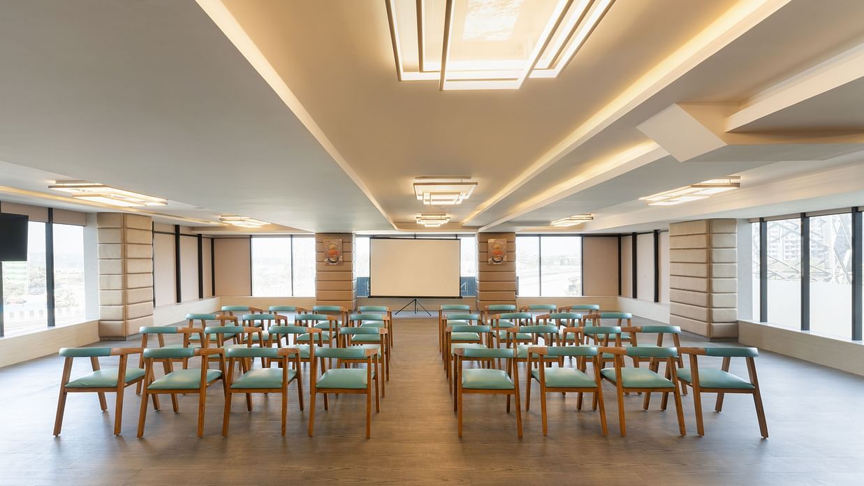 Modern conference hall with rows of wooden chairs facing a projector screen at Clarks Inn Suites, Hyderabad