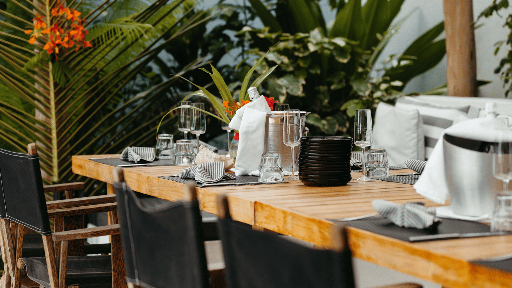 Spacious outdoor dining table with elegant setup amidst lush tropical plants.