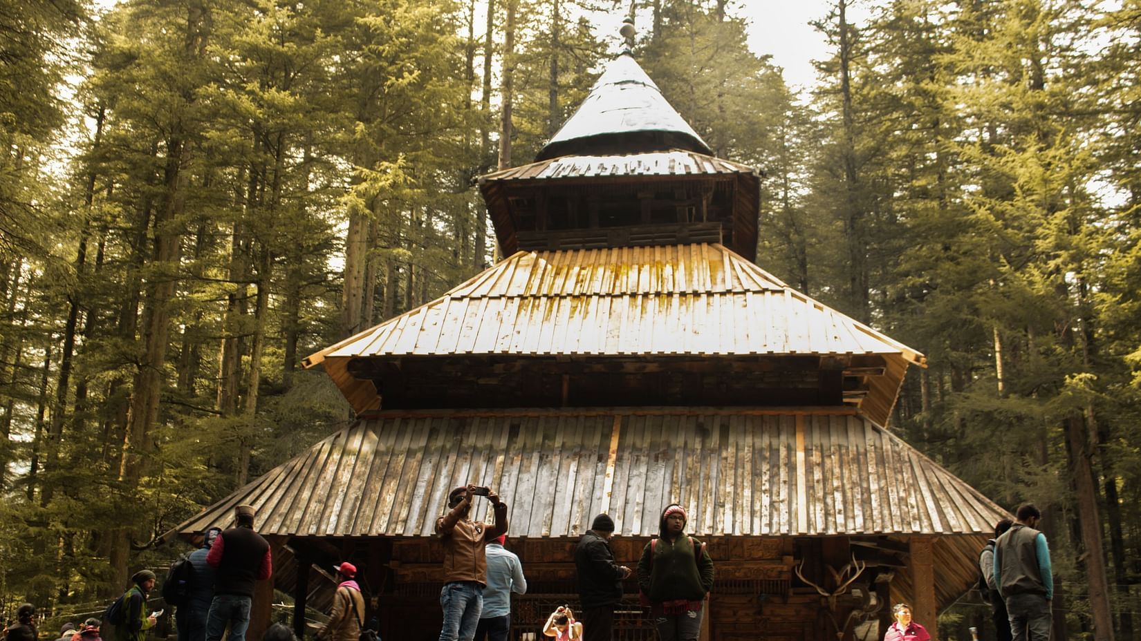 An image of people standing outside a temple with lush greenery around