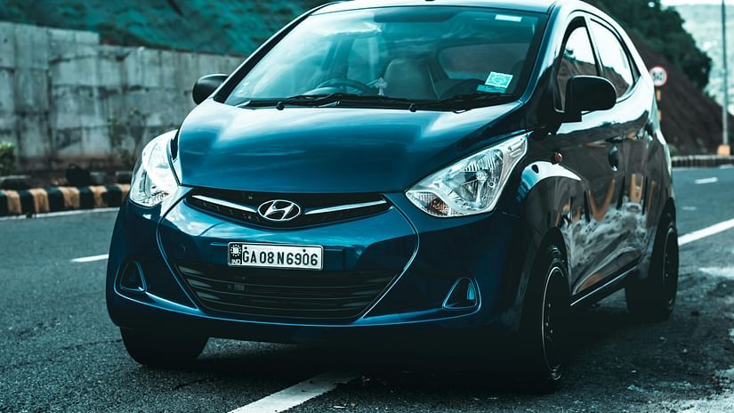 A blue Hyundai Eon with significant damage to its front end parked on the side of the road.
