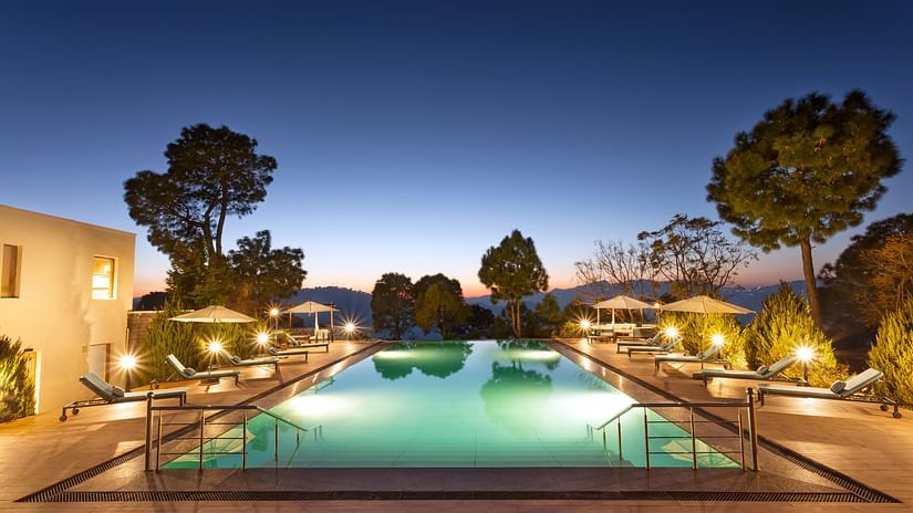 Image of a large swimming pool at Suryavilas in the evening as the premises are surrounded by trees
