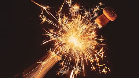 A champagne bottle popping with sparks in between the bottle's mouth and cork
