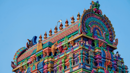 Close up of a temple gopuram against a clear blue sky in the background, with intricate patters and carvings on the structure.