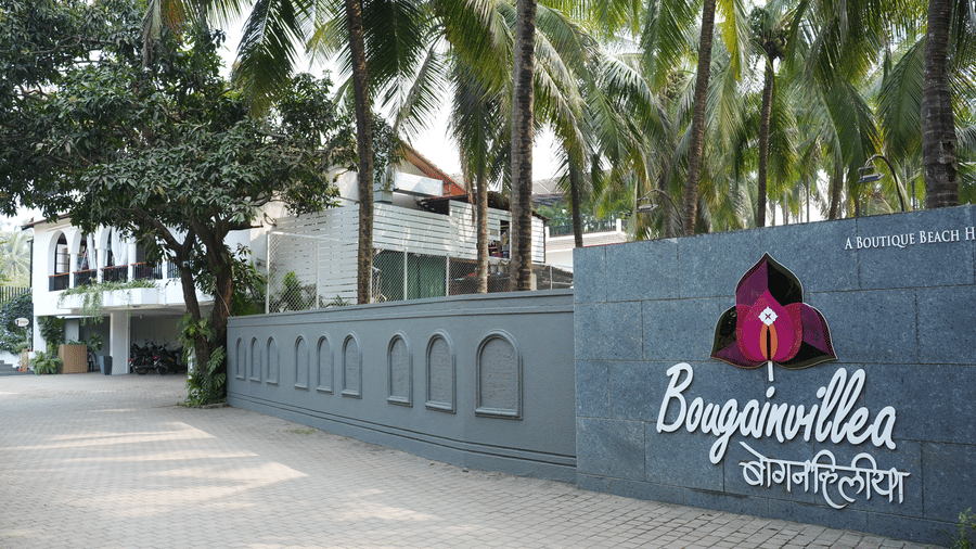 A stone entrance wall featuring a logo, the name Bougainvillea, and palm trees at Bougainvillea, Alibaug.
