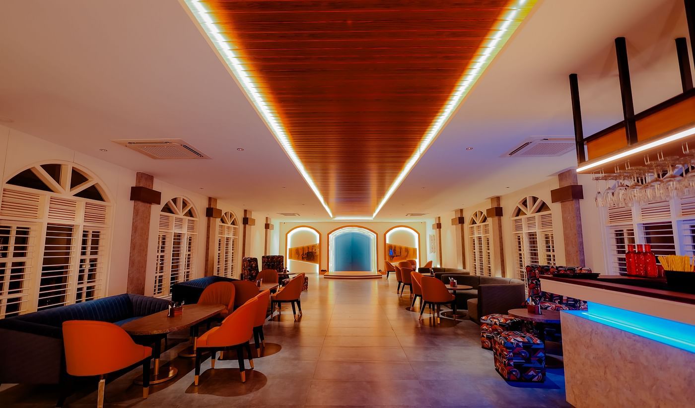 A long, brightly lit hallway with a bar area on the right, featuring colourful lighting and a modern design -  Nirantara Resort & Spa