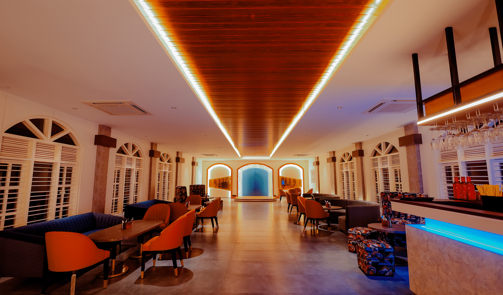 A long, brightly lit hallway with a bar area on the right, featuring colourful lighting and a modern design -  Nirantara Resort & Spa