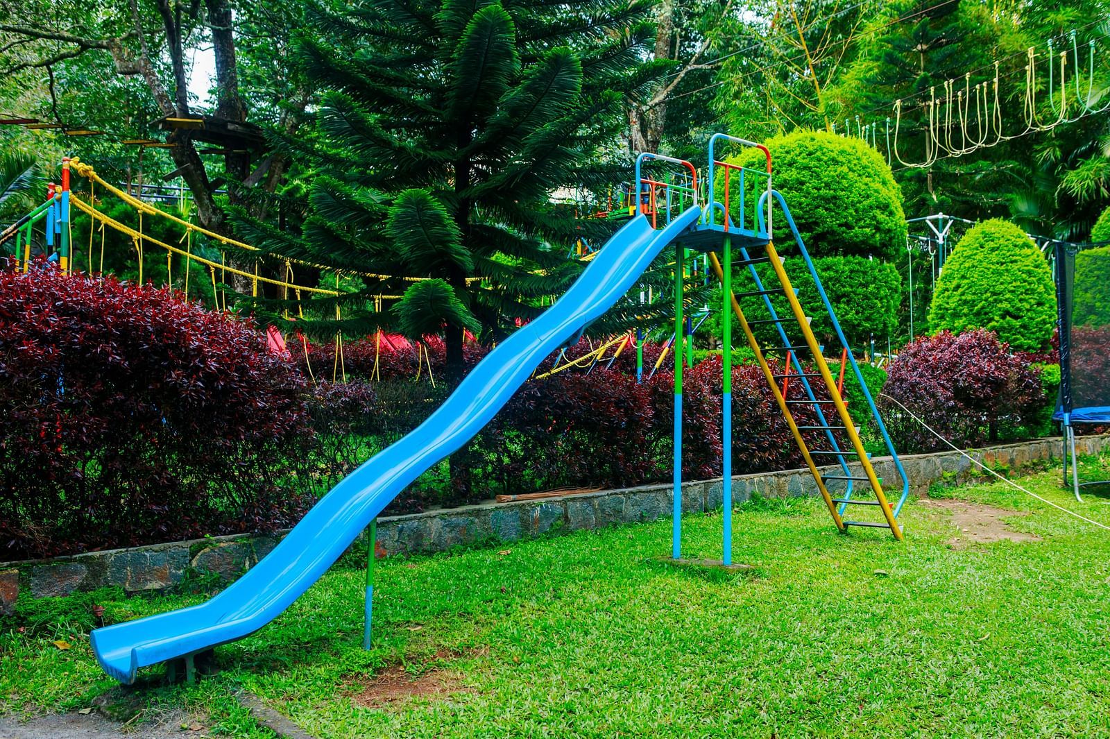 A brightly coloured blue slide in a lush green garden surrounded by neatly trimmed bushes and trees—an inviting outdoor play area at our child-friendly hotel in Yercaud, perfect for young guests to enjoy.