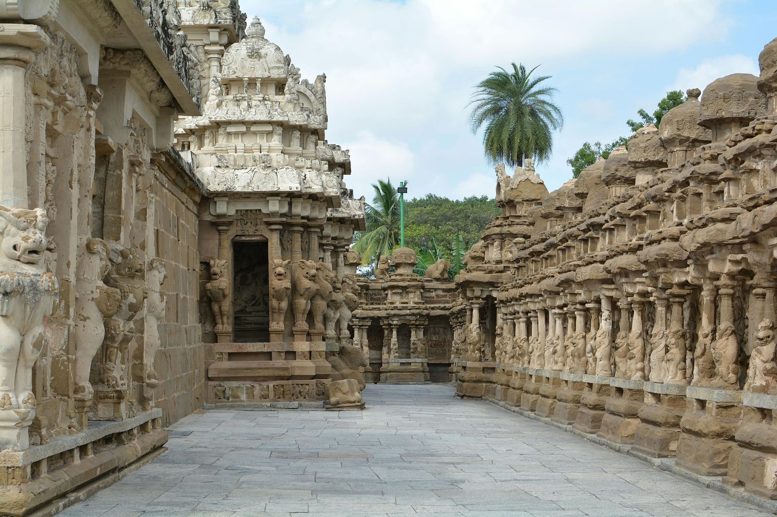 A view showing temple architecture inside a temple complex and also coconut trees in the background.