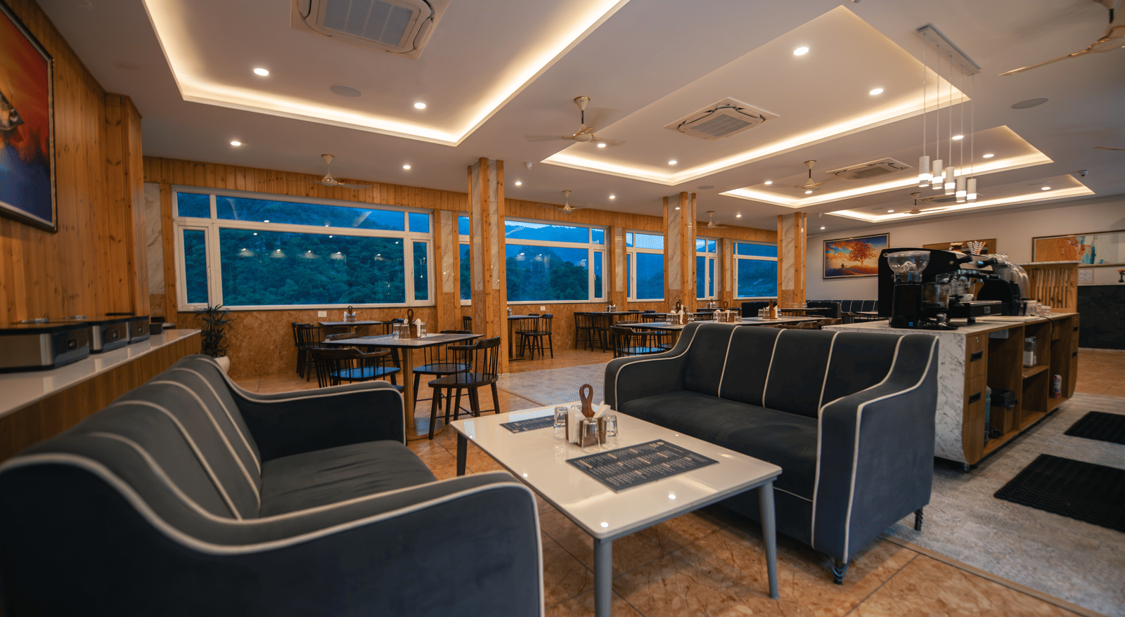 A restaurant at The Tattva Devaprayag with dark grey couches and a coffee table.