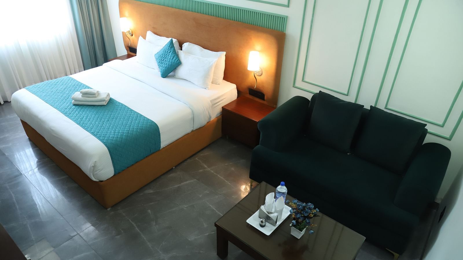 A room with a double bed featuring a blue and white design, alongside a dark coloured sofa - Asian Suites IFFCO Metro, Gurgaon