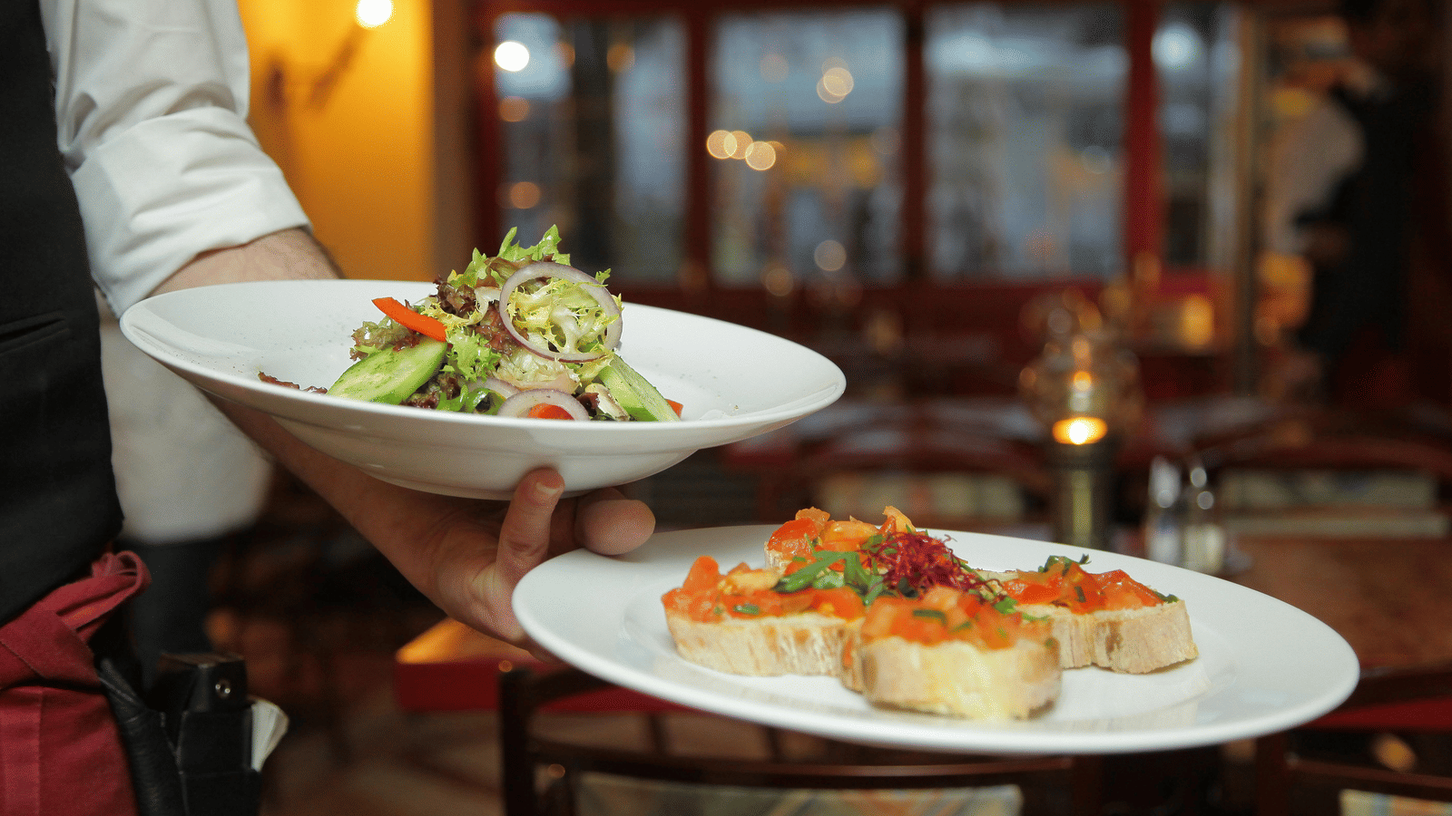 a person in a restaurant holding two plates with delicious cuisines in it that are well plated