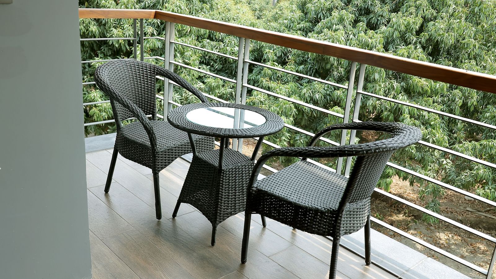 Cosy balcony setup with a round table and two wicker chairs overlooking lush foliage at Wyndham Garden.
