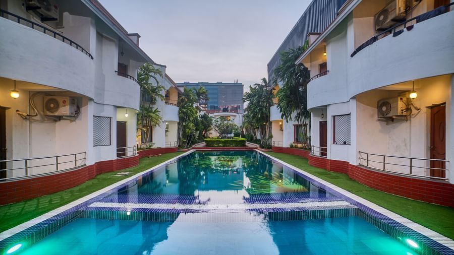 A symmetrical view of Ilara Hotels & Spa, OMR, Chennai illuminated at dusk, lining a long, reflective swimming pool or water feature.