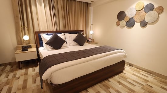 Side angle view of cozy view with bedside table and lamps illuminating the Deluxe King  - Mastiff Hotel, Dhanbad 