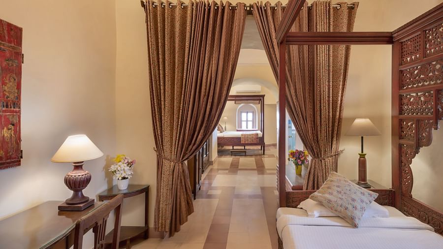 A room with a four-poster bed, a desk, and curtained doorways leading to another room in Tijara Fort-Palace - 19th Century, Alwar.