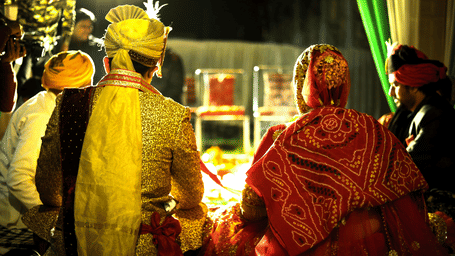 A couple dressed in yellow and red traditional Indian wedding attire attending the ceremony.