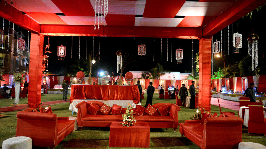 A fabric canopy standing over an outdoor lounge setup with red sofas and white tables on the lawn at Garh Govind.