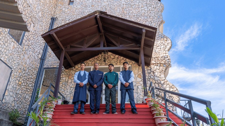 Four resort staff members standing on red-carpeted steps at the stone entrance of the building at Himalayas Resort By The Lake Hill, Mukteshwar.