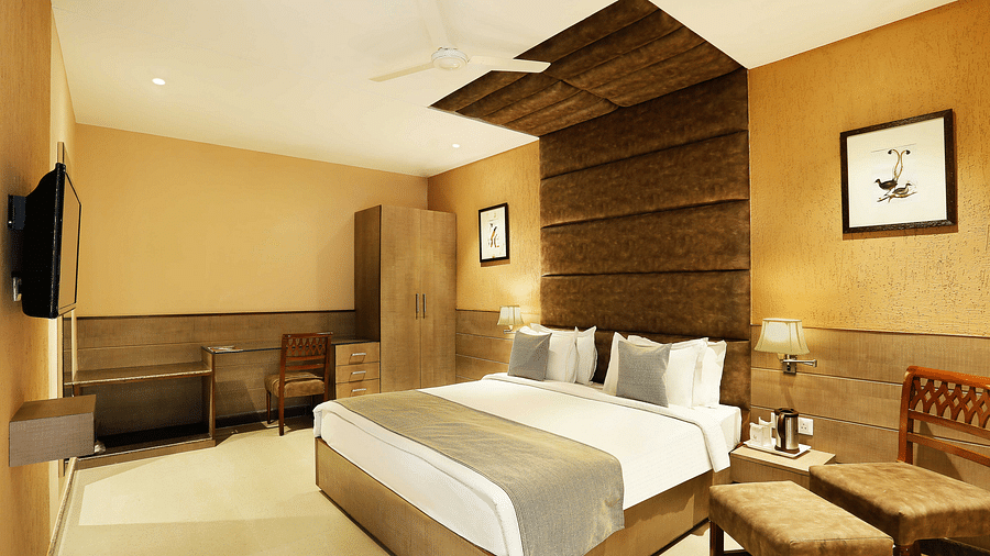 A bedroom at The Manor, Bareilly featuring a plush bed with a tufted headboard, a wall mounted television across from the bed, modern decor with soft lighting, and neutral tones 