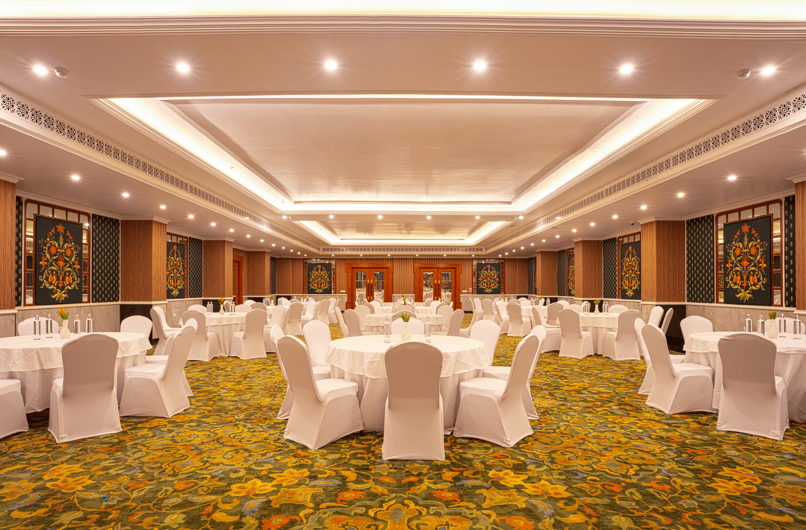 A large, elegant banquet hall with a patterned yellow carpet, set up with multiple circular tables and chairs at MAYFAIR Bay Resort, Paradeep.