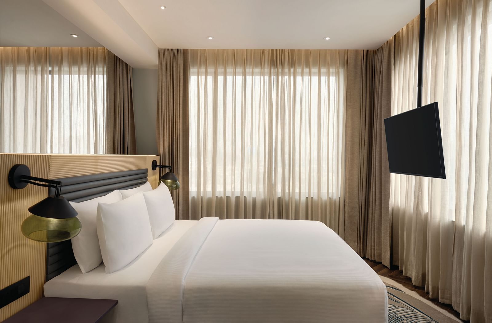 Ramada Encore by Wyndham, Bhiwadi |  Hotel bedroom with a white bed, TV, and large window with blinds.