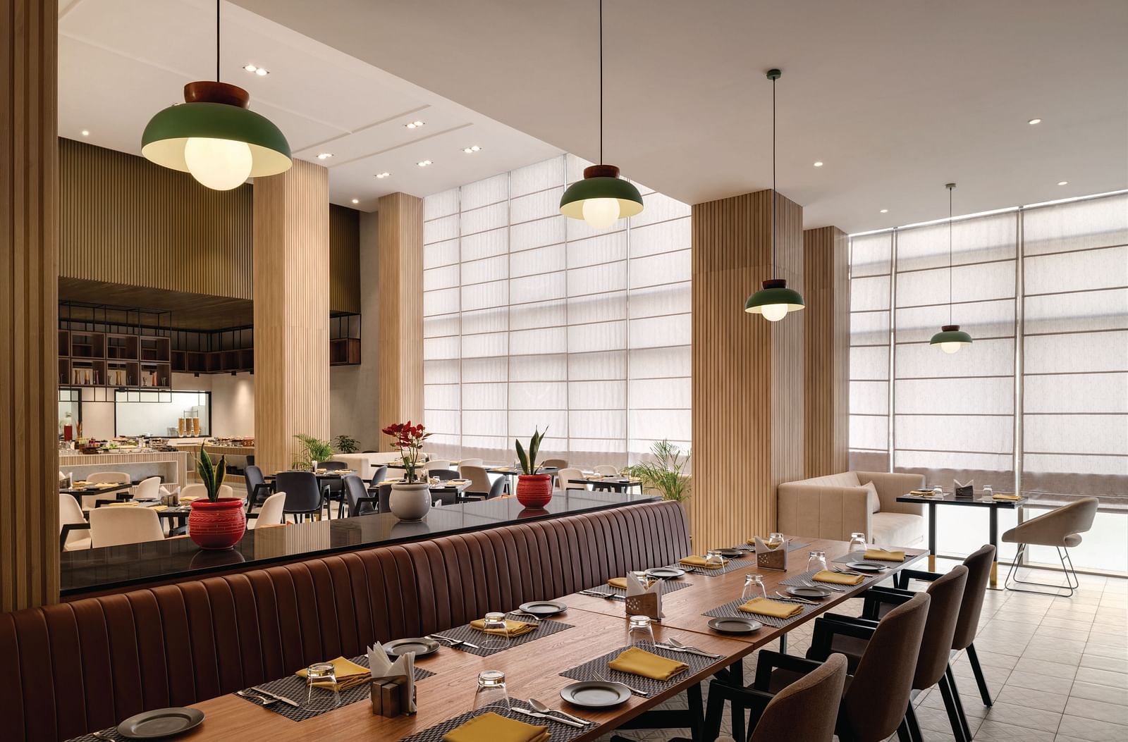 Ramada Encore by Wyndham, Bhiwadi | Restaurant with a long table, pendant lights, and a view of the kitchen.