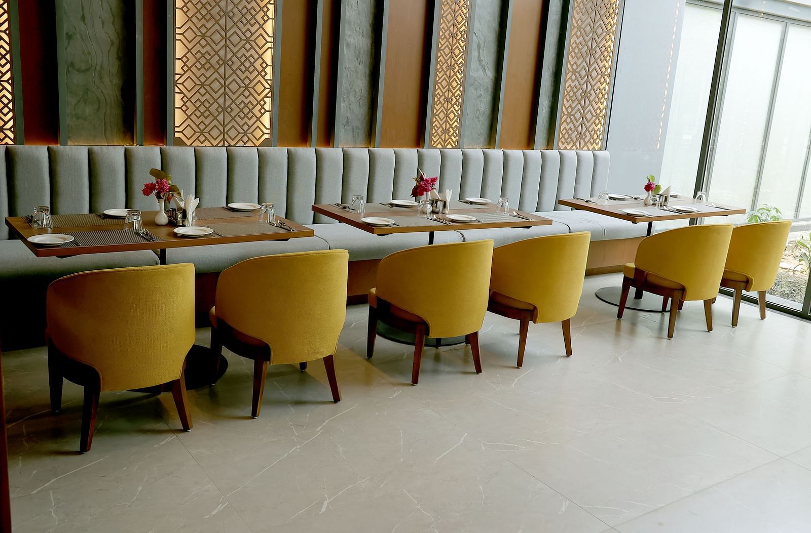 Elegant indoor dining area with mustard yellow chairs and a striped cushioned bench against a decorative wall at Wyndham Garden.
