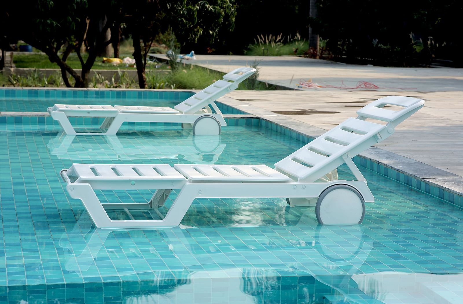 White sun loungers partially submerged in a turquoise pool, surrounded by trees and a stone deck at Wyndham Garden.