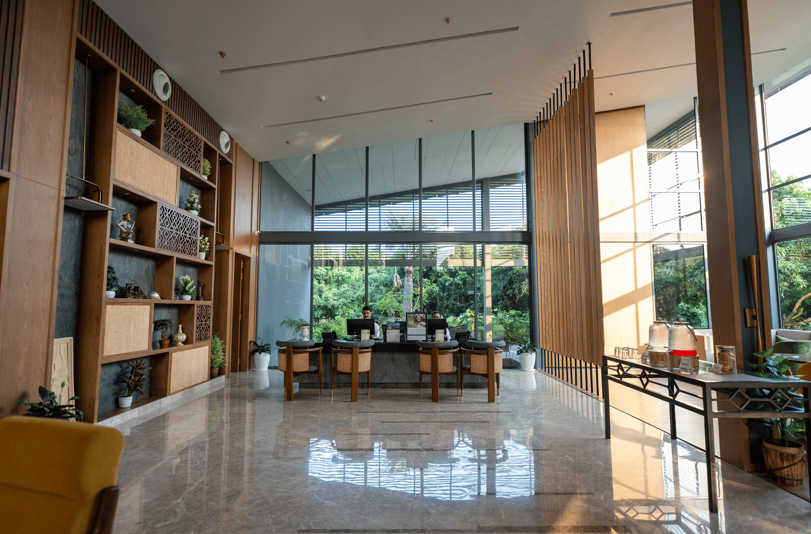 A grand lobby at Wyndham Garden with high ceilings, tall vertical panels, a long reception desk, expansive glass walls offering outdoor views, and natural light illuminating the polished floor.