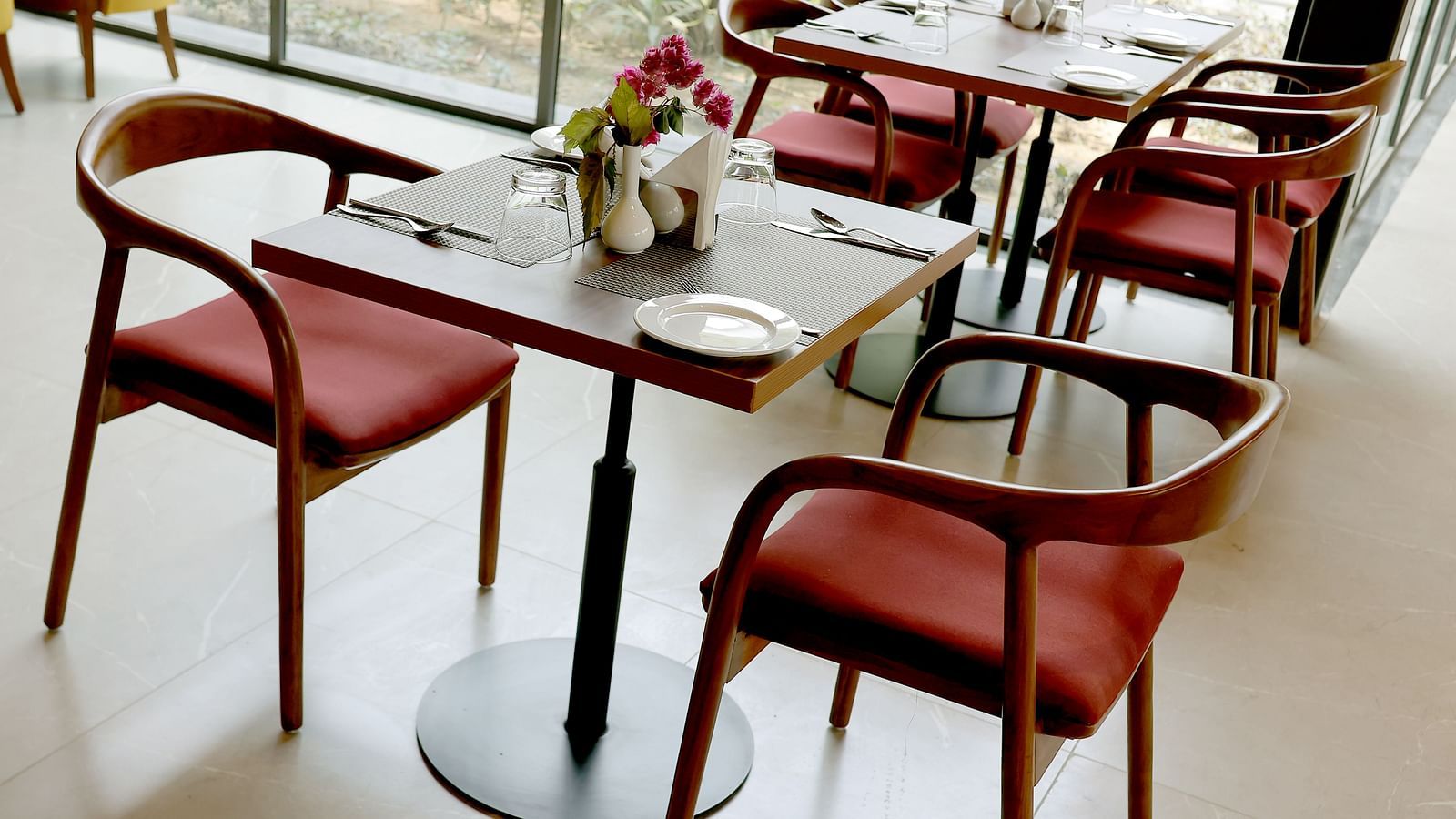 Modern dining setup with red-cushioned wooden chairs and neatly arranged tableware near glass walls at Wyndham Garden.
