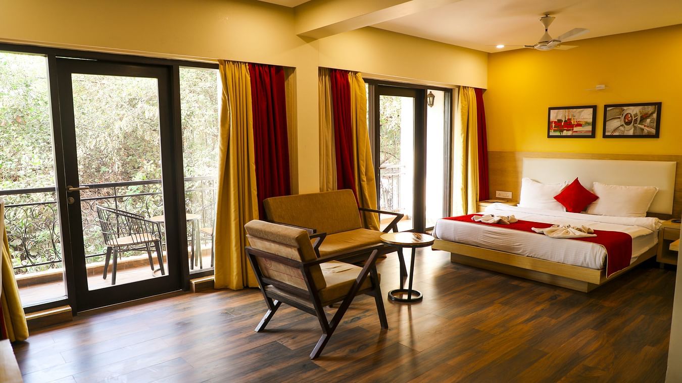 An overview of the Executive Suite with a double bed, chairs and balcony in view - Rosetum Anjuna.