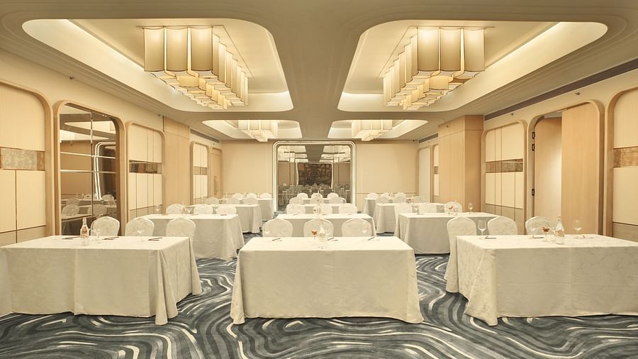 Event space featuring several rectangular tables draped in white. Beige chairs are placed around them. Patterned floor - The Orchid Hotel, Chandigarh