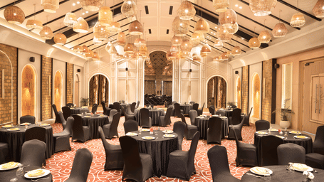 Banquet hall at Polo Resort Cherrapunji with woven pendant lights, round tables with black covers, arched alcoves and red patterned carpet.