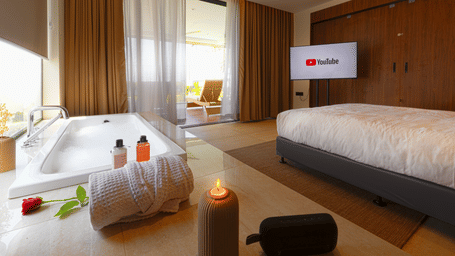 A bedroom at hotel SUKAVI with a king size bed, a television, and an open bathtub area near a window balcony.