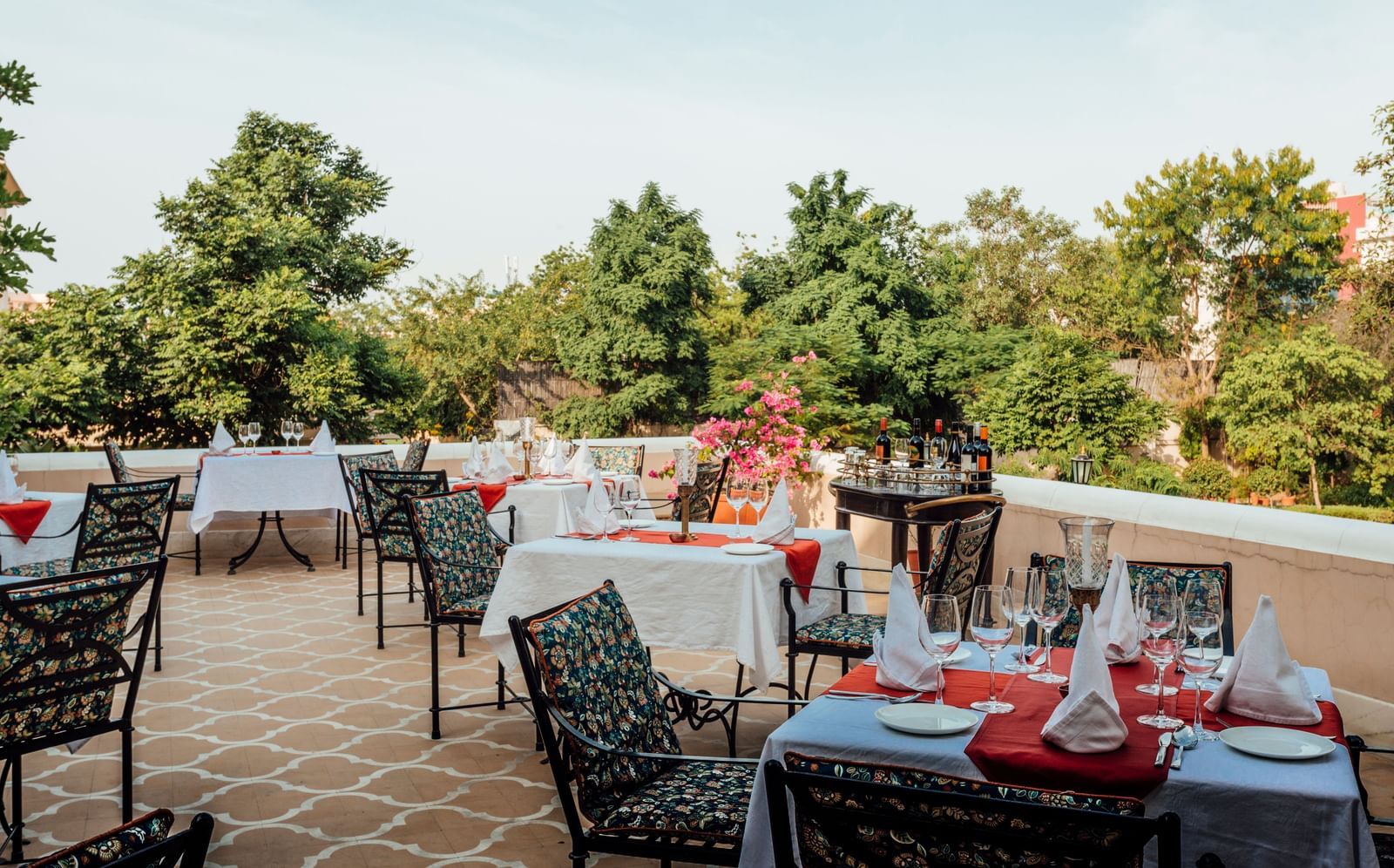 An outdoor dining terrace at Royal Heritage Haveli with tables set, overlooking trees and a distant landscape.