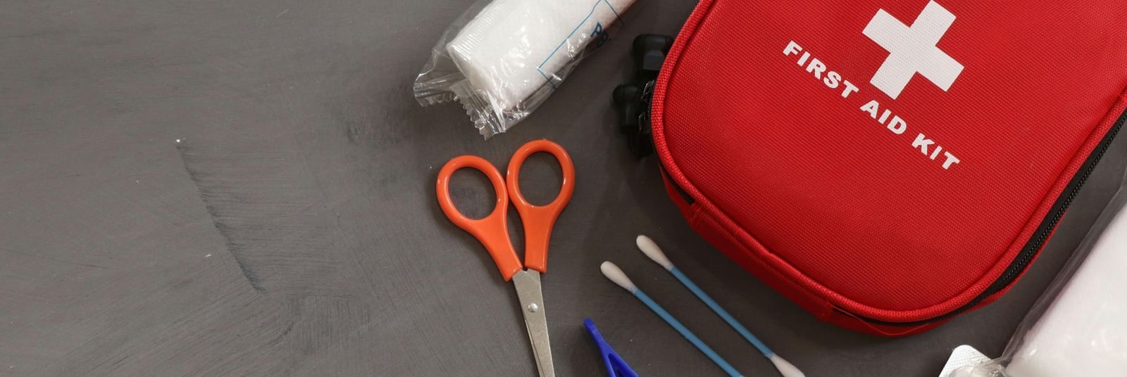 A red coloured pouch reading 'First Aid Kit' with several items and medicines scattered around it.