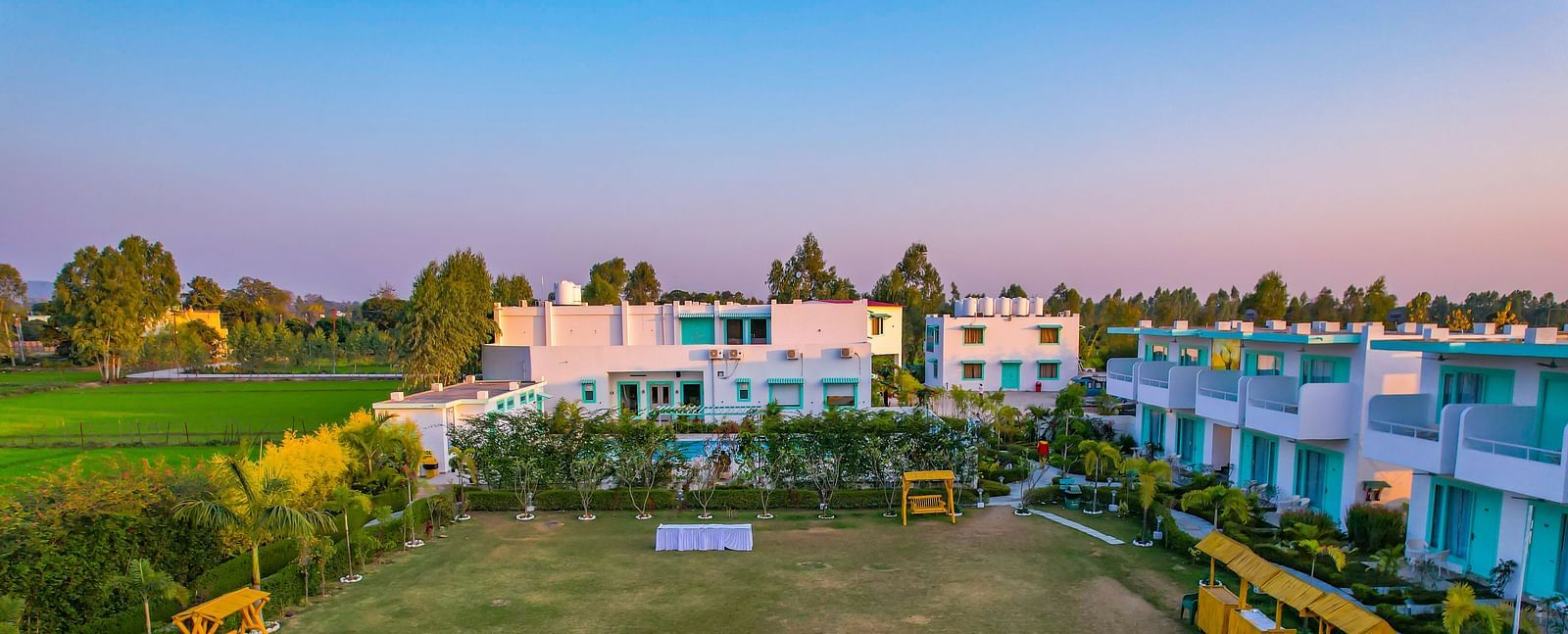 Lawn area at Vedikant Resorts The Mallard Corbett with tables and chairs set up outdoors, bordered by hedges and facing the rooms.
