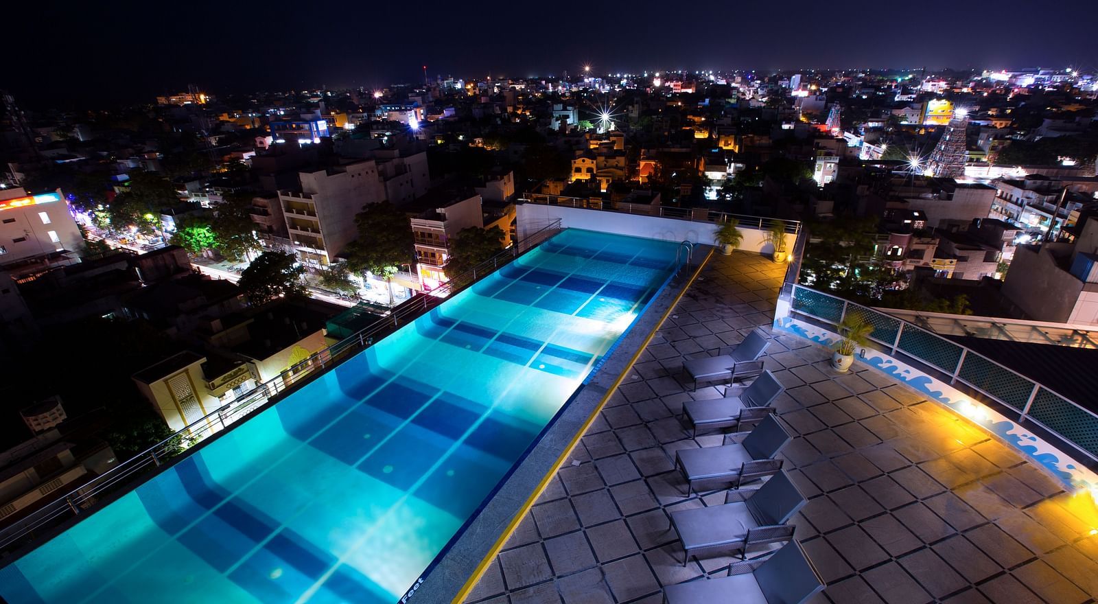 Rooftop Pool with lounging chairs during the night at Hotel Atithi - TGI Grand, Pondicherry