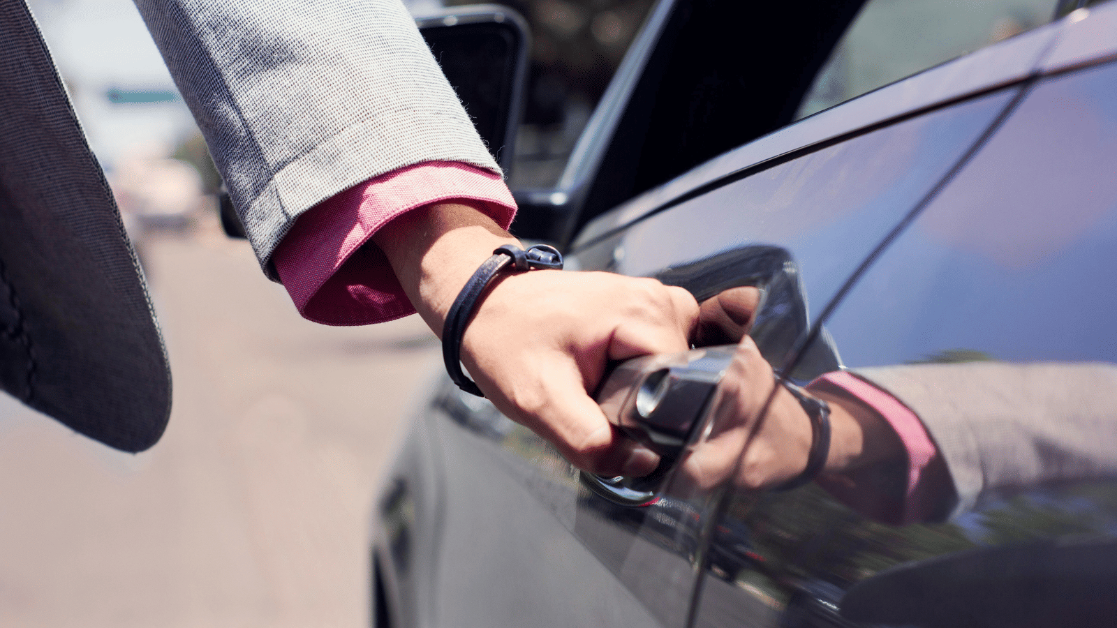 A person dressed in business formals opening the door of a car.