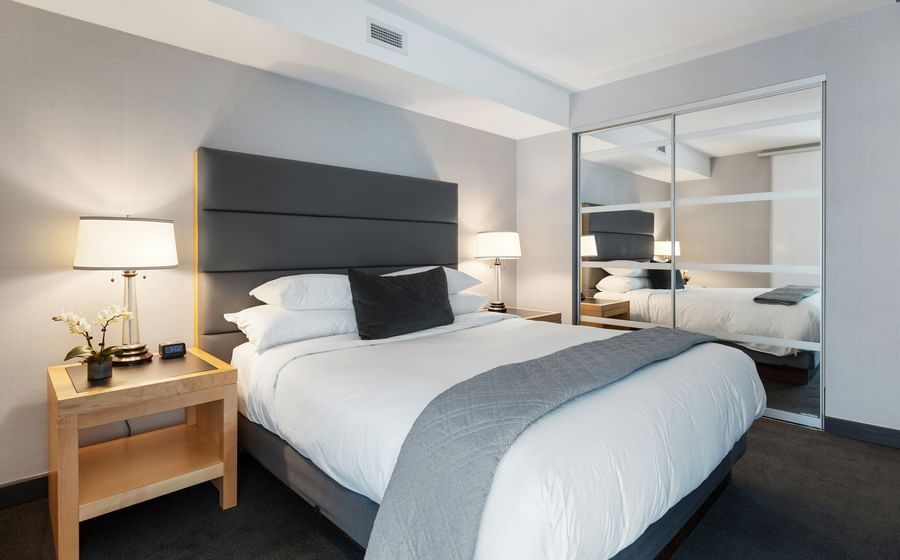 A modern hotel room with a double bed, a table with a lamp beside it and a huge mirror.