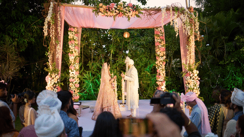 A bride and groom under a canopy during their wedding ceremony with a crowd looking on - Heritage Village Resorts & Spa, Goa
