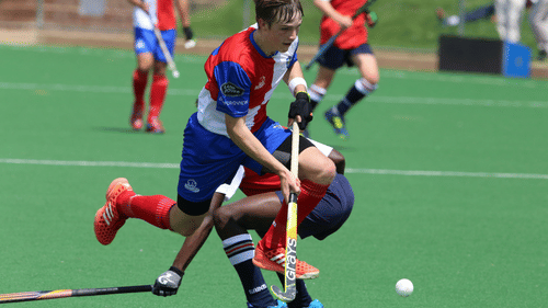 A field hockey match with two players in action on the field, one player tackling the other near the ball.