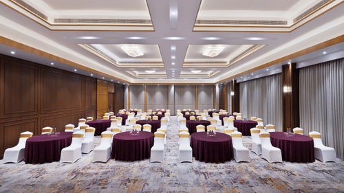 Indoor ballroom at Royal Tulip Shivapuri National Park - Kathmandu featuring round tables with linens and rows of white chairs.