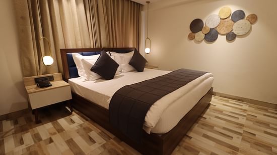 Side angle view of cozy view with bedside table and lamps illuminating the Deluxe King  - Mastiff Hotel, Dhanbad 