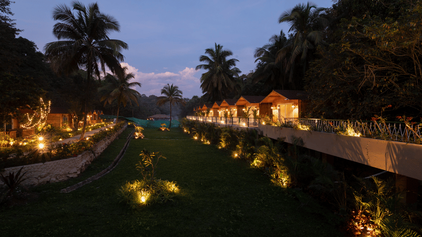 Evening scene with beautifully lit cottages and lush green surroundings. | Stone Wood Jungle Resort, Dandeli