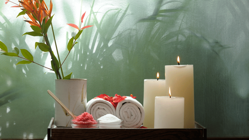 Candles and a floral arrangement set against a green wall with leafy shadows at Amanvana Spa Resort.