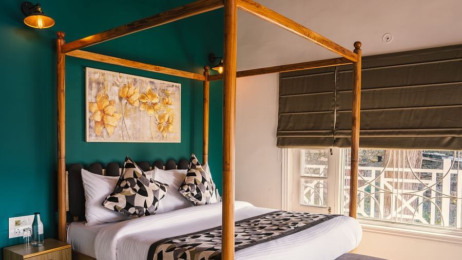 A spacious bed with a wooden frame, a photo frame above the headboard, and a half-closed window to the side at BluSalzz Villas - The Green Roof, Bhimtal.