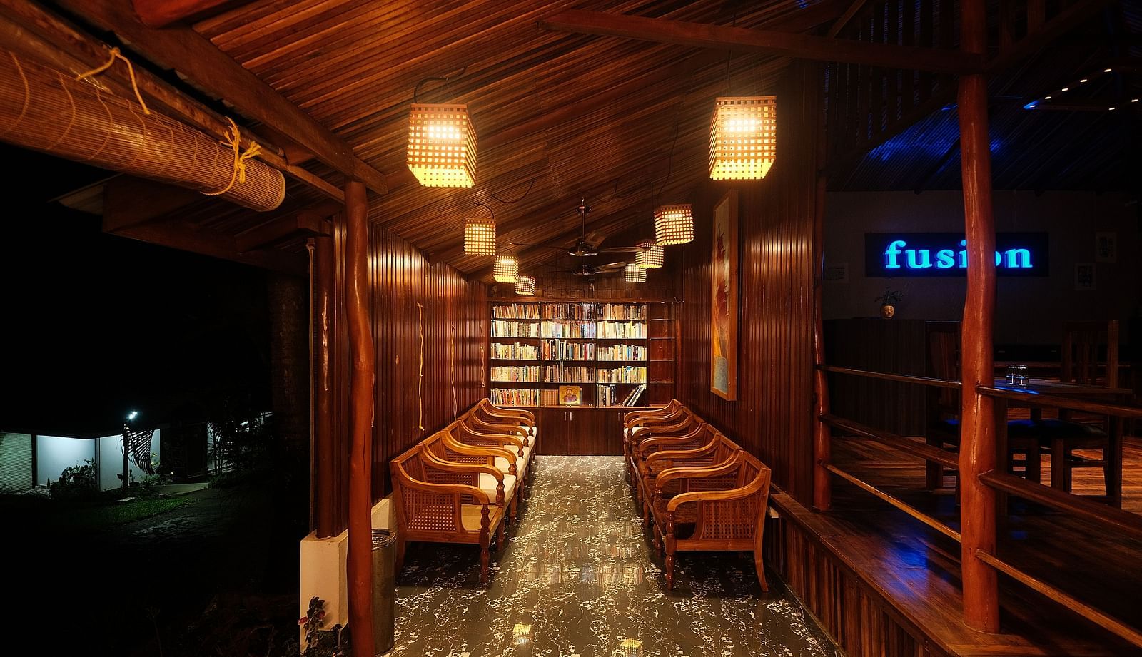 A dimly lit wooden interior features rows of seating and shelves, illuminated by hanging lamps | Fusion Cafe and Multi-cuisine | RainForest Resort, Port Blair, Andaman and Nicobar Island